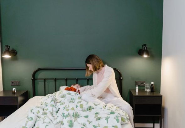 A mother cares for her child with a fever in a warm, cozy bedroom setting.