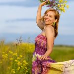 A smiling woman in a vibrant dress holding flowers in a sunny meadow