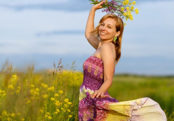 A smiling woman in a vibrant dress holding flowers in a sunny meadow